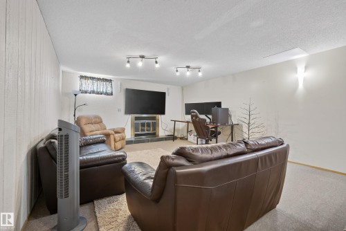 Spacious room featuring paneled walls, recessed lighting, and a fireplace with a black tile surround - 10935 152 Street, Edmonton, AB 