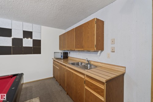 Equipped kitchenette featuring wood-finish cabinetry, a double basin sink, and laminate countertops - 10935 152 Street, Edmonton, AB 