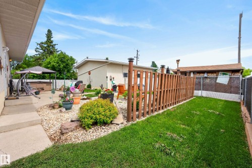 Expansive backyard featuring a manicured lawn, concrete patio, a gravel landscape bed, and a vertical wood-slat privacy fence - 10935 152 Street, Edmonton, AB 
