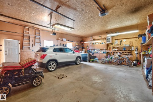 Spacious garage featuring a concrete floor, built-in cabinetry, wall shelving, and multiple fluorescent light fixtures - 10935 152 Street, Edmonton, AB 