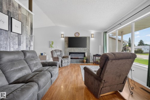 Spacious living area featuring wood-finish flooring, a vaulted ceiling, and an accent wall with vertical paneling - 10935 152 Street, Edmonton, AB 