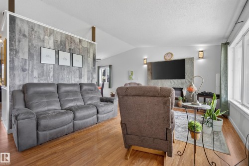 Living space featuring wood-finish flooring, vaulted ceilings, and a stone-clad fireplace surround with flanking sconce lighting - 10935 152 Street, Edmonton, AB 