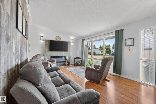 Living area featuring wood-finish flooring, a contemporary fireplace with stone surround, a prominent picture window, and a vaulted ceiling with textured finish - 10935 152 Street, Edmonton, AB 