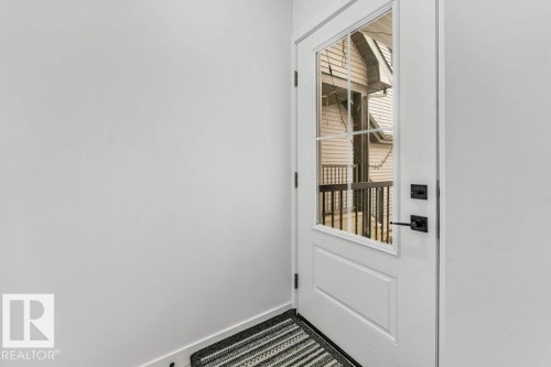 White entry door with a divided light window and matte black hardware, featuring a partial view of an exterior porch with wood siding - 423 28 Street, Edmonton, AB 
