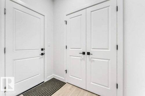 Entryway featuring light wood-finish flooring, white paneled doors, and matte black hardware - 423 28 Street, Edmonton, AB 
