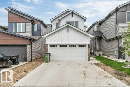 Contemporary two-story residence with a white garage door featuring upper window panels, stone accents, and vertical white siding - 423 28 Street, Edmonton, AB 