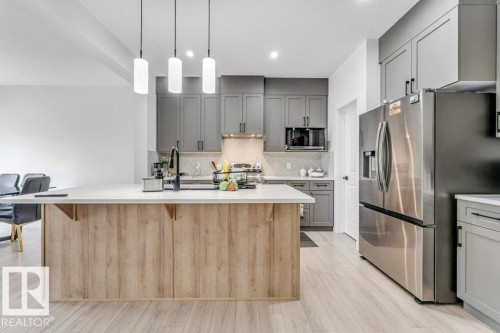 Kitchen featuring a light wood-finish island with a white countertop, gray shaker-style cabinetry, and stainless steel appliances - 423 28 Street, Edmonton, AB 