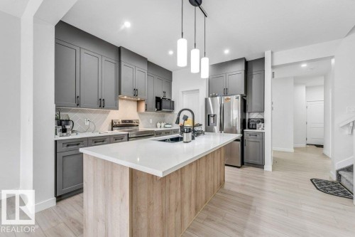 Modern kitchen featuring gray cabinetry, a central island with wood-finish paneling and a light-colored countertop, stainless steel appliances, and wood-finish flooring - 423 28 Street, Edmonton, AB 