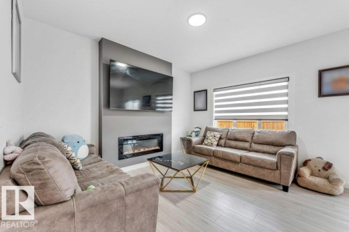 Living area featuring a modern electric fireplace with a dark surround, recessed ceiling lighting, and light wood-finish flooring - 423 28 Street, Edmonton, AB 