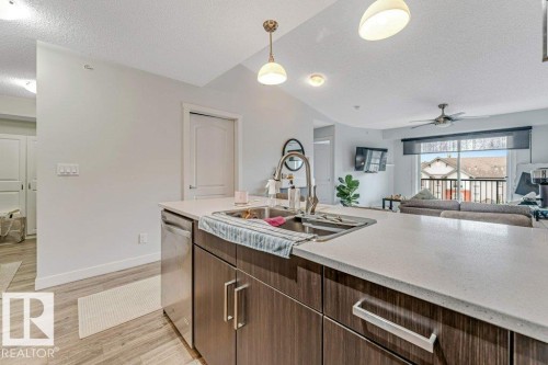 Kitchen island with light-toned countertop and wood-finish cabinetry, featuring a stainless steel undermount sink and integrated dishwasher - 401 667 Watt Boulevard, Edmonton, AB 