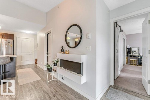 Modern entryway featuring wood-finish flooring, a contemporary electric fireplace, and a barn door entry to a separate space - 401 667 Watt Boulevard, Edmonton, AB 
