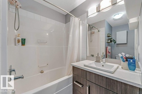 Bathroom featuring a shower-tub combination with white tile surround, a vanity with a rectangular sink, wood-finish cabinetry, and a light-colored countertop - 401 667 Watt Boulevard, Edmonton, AB 