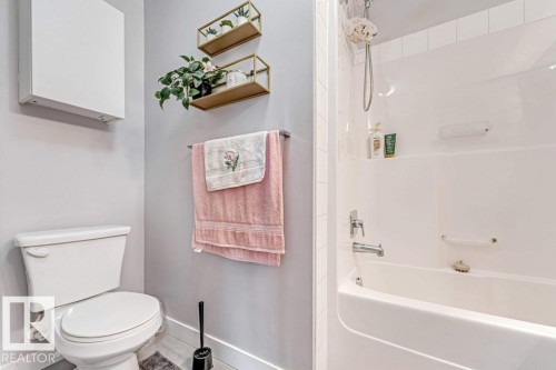 Full bathroom featuring a white toilet, white built-in wall cabinet, and a white tub/shower combination with a chrome faucet - 401 667 Watt Boulevard, Edmonton, AB 