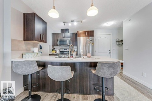 Modern kitchen featuring dark wood-finish cabinetry, stainless steel appliances, and a central island with a light-toned countertop - 401 667 Watt Boulevard, Edmonton, AB 