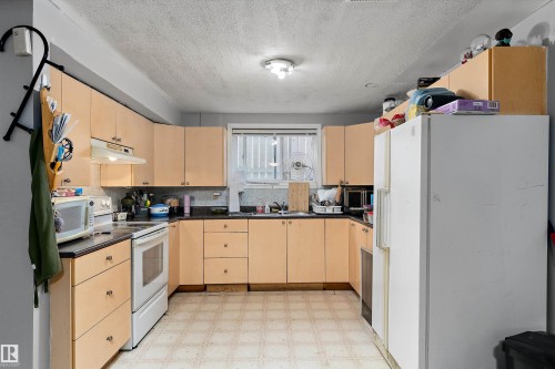 Kitchen featuring light wood-finish cabinetry, dark countertops, and a white oven with an overhead range hood - 14707 33 Street, Edmonton, AB 