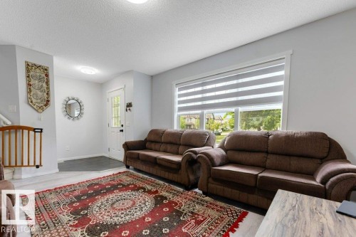 Inviting living space featuring light wood-finish flooring, a prominent window with horizontal blinds, and a white entrance door with decorative glass - 3511 15A Street, Edmonton, AB 