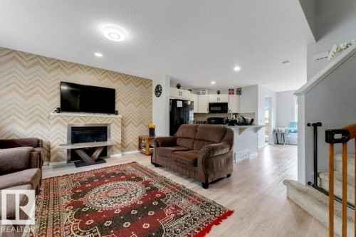 Living area featuring a chevron-patterned accent wall, a built-in fireplace, recessed lighting, and wood-finish flooring - 3511 15A Street, Edmonton, AB 