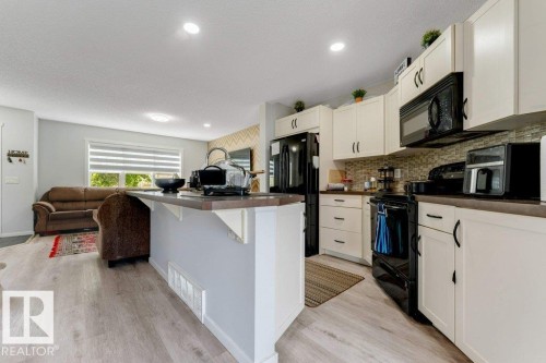 Modern kitchen featuring light cabinetry, black appliances, a tile backsplash, and a breakfast bar - 3511 15A Street, Edmonton, AB 