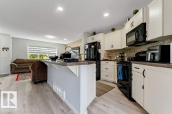 Modern kitchen featuring light cabinetry, black appliances, a tile backsplash, and a breakfast bar - 