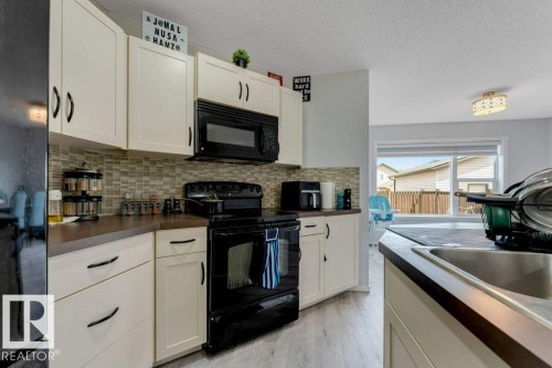 Kitchen featuring cream-toned cabinetry with dark hardware, dark countertops, a mosaic tile backsplash, black appliances, and light wood-finish flooring - 3511 15A Street, Edmonton, AB 
