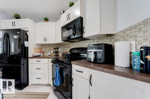 Kitchen featuring white cabinetry with dark hardware, dark countertops, and a full tile backsplash - 3511 15A Street, Edmonton, AB 