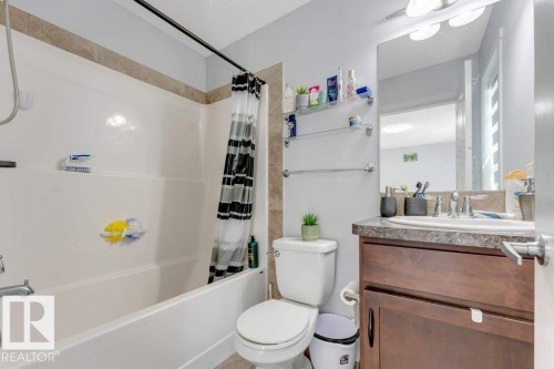 Bathroom featuring a white tub, shower with tiled surround, wood-finish vanity with countertop, integrated sink, and wall-mounted mirror with overhead lighting - 3511 15A Street, Edmonton, AB 