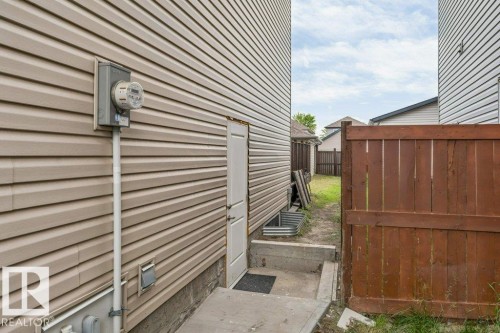 Beige horizontal siding with a white utility door, concrete foundation, and a partial wooden privacy fence - 3511 15A Street, Edmonton, AB 