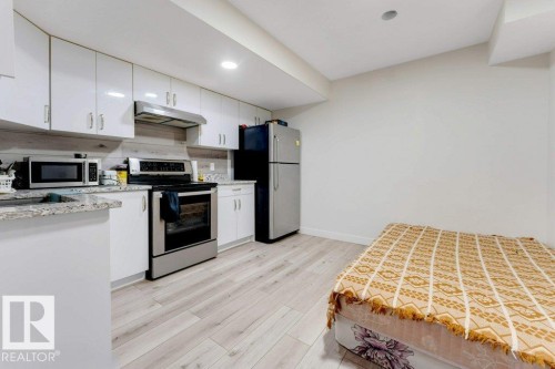 Compact kitchen area featuring white cabinetry, light-toned wood-finish flooring, stainless steel range and range hood, and a light-colored countertop - 3511 15A Street, Edmonton, AB 