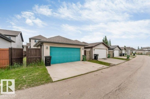 Detached rear garage featuring a vibrant teal overhead door, concrete driveway, and neutral siding - 3511 15A Street, Edmonton, AB 