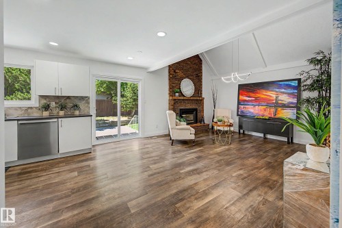 Open-concept living space featuring wood-finish flooring, a brick-surround fireplace, and vaulted ceilings with exposed beams - 3718 103B Street Nw, Edmonton, AB - Indoor With Fireplace
