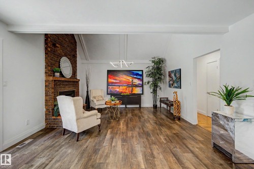 Spacious living area featuring a prominent exposed brick fireplace, high vaulted ceilings with white beams, and wood-finish flooring - 3718 103B Street Nw, Edmonton, AB - Indoor With Fireplace