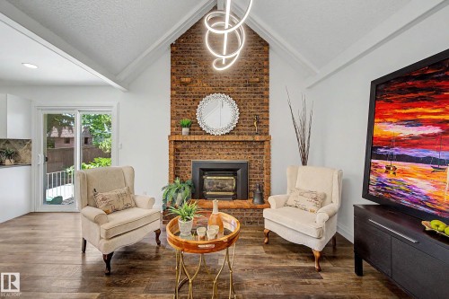 Vaulted ceilings with a unique linear light fixture, brick-clad fireplace with wood mantle, wood-finish flooring, and sliding glass doors to the exterior - 3718 103B Street Nw, Edmonton, AB - Indoor Photo Showing Living Room With Fireplace