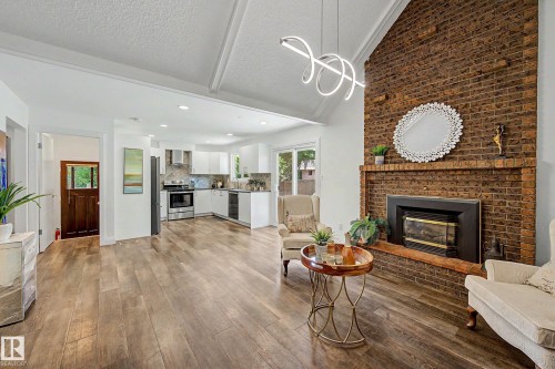 Vaulted ceiling great room with a floor-to-ceiling brick fireplace, wood-finish flooring, and a contemporary linear chandelier - 3718 103B Street Nw, Edmonton, AB - Indoor Photo Showing Living Room With Fireplace