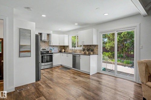 Open-concept kitchen featuring white cabinetry, stainless steel appliances, wood-finish flooring, recessed lighting, and sliding glass doors to the exterior - 3718 103B Street Nw, Edmonton, AB - Indoor Photo Showing Kitchen With Upgraded Kitchen