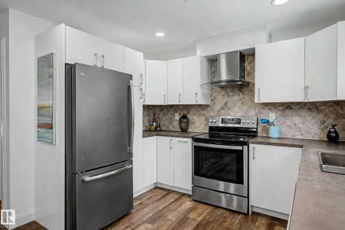 Kitchen featuring white cabinetry with silver hardware, wood-finish flooring, and a patterned tile backsplash - 3718 103B Street Nw, Edmonton, AB - Indoor Photo Showing Kitchen With Double Sink