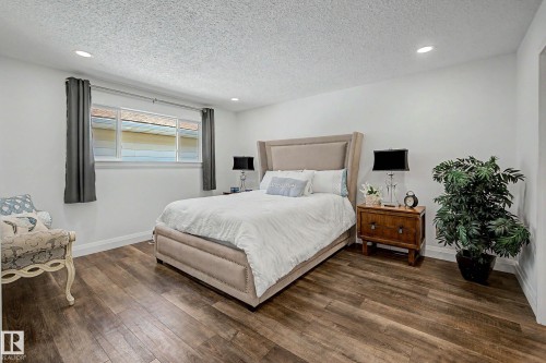 Spacious room featuring wood-finish flooring, white walls, and a large window with gray drapes - 3718 103B Street Nw, Edmonton, AB - Indoor Photo Showing Bedroom