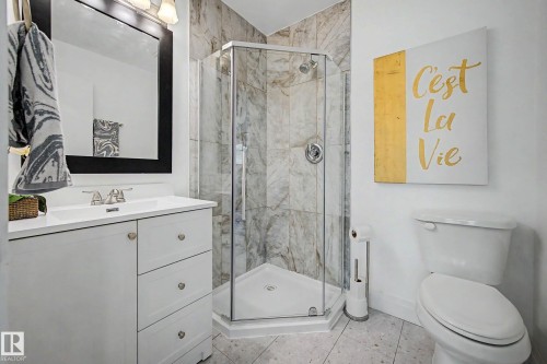 Bathroom featuring a corner glass-enclosed shower with marble-look tile surround, a single vanity with a white countertop, and mosaic-style floor tiling - 3718 103B Street Nw, Edmonton, AB - Indoor Photo Showing Bathroom