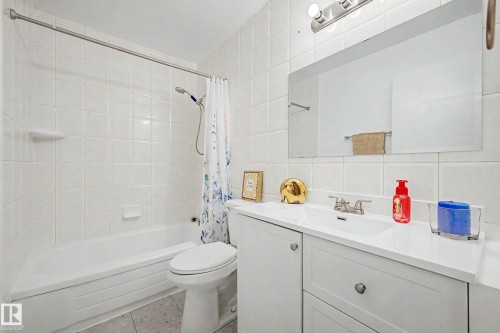 Full bathroom featuring a white porcelain tub with shower, white square wall tiling, and a vanity with an integrated sink and base cabinetry - 3718 103B Street Nw, Edmonton, AB - Indoor Photo Showing Bathroom