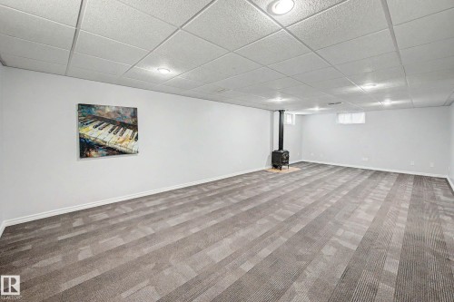 Spacious room featuring gray patterned carpeting, white walls, recessed ceiling lighting, and a black wood-burning stove - 3718 103B Street Nw, Edmonton, AB - Indoor