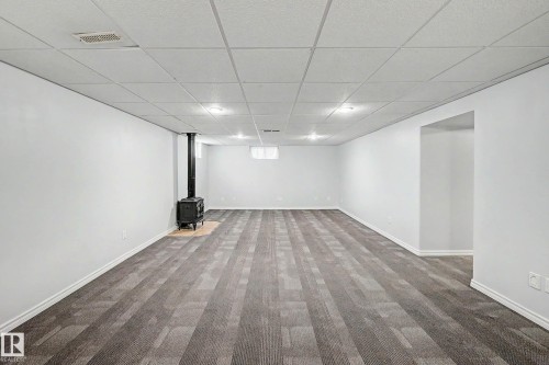 Spacious finished lower level featuring a freestanding wood stove, recessed lighting, drop ceiling, and gray wood-finish flooring - 3718 103B Street Nw, Edmonton, AB - Indoor Photo Showing Other Room