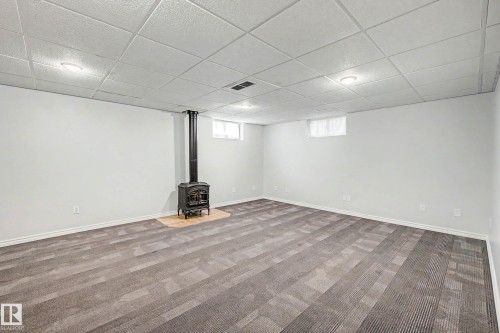 Spacious room featuring a central wood-burning stove with a light-toned hearth - 3718 103B Street Nw, Edmonton, AB - Indoor