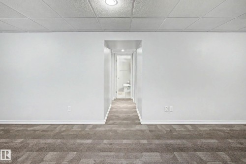 Spacious room featuring neutral carpeting with a geometric pattern, crisp white walls, and a suspended acoustic tile ceiling with recessed lighting - 3718 103B Street Nw, Edmonton, AB - Indoor Photo Showing Other Room