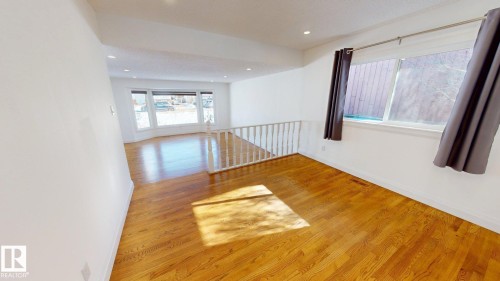 Hardwood flooring spanning the open-concept space, featuring white walls and a white railing - 3718 103B Street, Edmonton, AB 