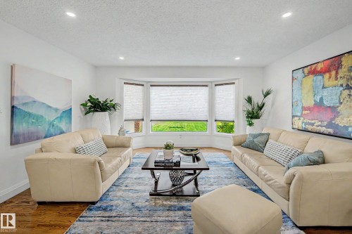 Sunlit living area featuring a bay window with multiple panes, recessed lighting, wood-finish flooring, and crisp white walls - 3718 103B Street Nw, Edmonton, AB - Indoor Photo Showing Living Room