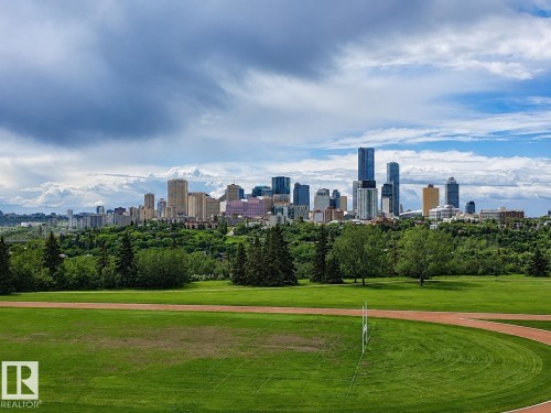 Expansive green space featuring a track, bordered by mature trees and a distant cityscape - 10415 84 Street, Edmonton, AB 