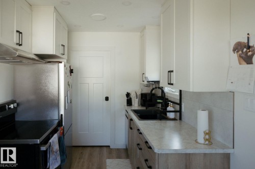 Contemporary kitchen featuring white upper cabinetry and wood-finish lower cabinetry with dark hardware - 10503A 109 Street, Westlock, AB - Indoor Photo Showing Kitchen With Double Sink