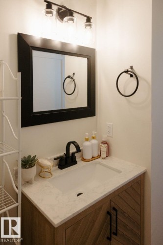 Bathroom vanity featuring a light-toned countertop with an integrated sink, matte black faucet, and a wood-finish cabinet with chevron-patterned doors - 10503A 109 Street, Westlock, AB - Indoor Photo Showing Bathroom