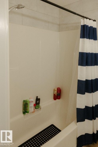 Bathtub-shower combination featuring a chrome showerhead, white tile surround, and a coordinating shower rod - 10503A 109 Street, Westlock, AB - Indoor Photo Showing Bathroom