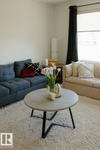 Bright living area featuring a round coffee table with a light-toned surface and black base, complemented by a plush area rug - 10503A 109 Street, Westlock, AB - Indoor Photo Showing Living Room