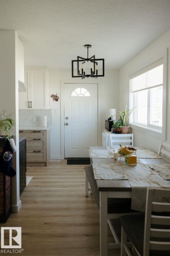 Open-concept living space featuring wood-finish flooring, a contemporary black geometric chandelier, white shaker-style cabinetry with matte black hardware, a white subway tile backsplash, and a white entry door with an arched window insert - 10503A 109 Street, Westlock, AB - Indoor Photo Showing Dining Room